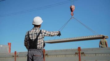 A foreman in a hard hat signals to a crane operator while lifting a concrete slab at a busy construction site video