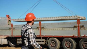 A construction foreman wearing a hard hat coordinates the placement of a concrete slab lifted by a crane video