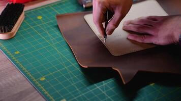 Close-up of a craftsman marking a leather sheet using a perforated template and an awl video