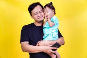 A happy fahter holds their child, both smiling against a bright yellow background. fathers day concept photo