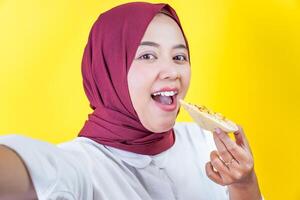smiling asian woman take selfie while eating pizza on yellow background photo