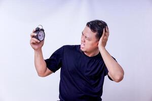 An asian man shocked by the alarm clock, expressing frustration over time management isolated on white background photo