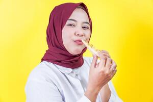 A beautyful asian woman in a hijab enjoys a slice of pizza against a bright yellow background photo