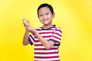 A cheerful boy in a striped shirt happily holds a snack against a vibrant yellow background. international foods day concept photo