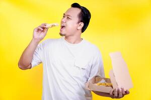 A man joyfully enjoys a slice of pizza against a bright yellow background. international foods day concept photo