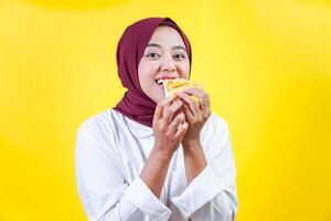 asian woman in a hijab enjoying while eating pizza on yellow background photo