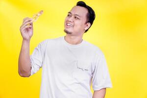A man smiles joyfully while holding a slice of pizza against a bright yellow background. international foods day concept photo