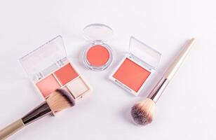open packs with peach-tone blush and various light tones on a white background with two professional makeup brushes. top view. decorative cosmetics photo