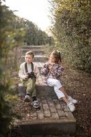 A boy and girl sit side by side on the steps, cameras in hand, capturing the world through curious eyes. photo