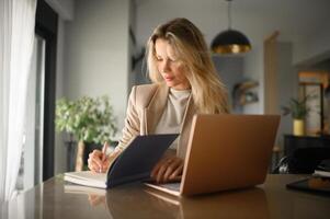 Sunlight streams through the windows as a blonde professional multitasks with her laptop and notebook. photo