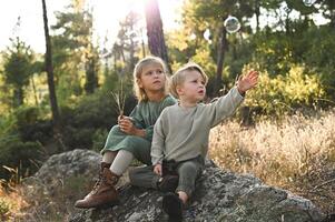 Hidden in the heart of a mystical forest, two children sit on a rock, reaching out to touch the delicate soap bubbles floating by. photo