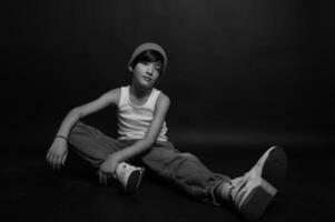 Dressed simply in jeans and a white tank top, a young Asian boy poses confidently in a studio, the dark background emphasizing his presence and expression. photo
