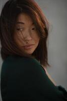 The golden hour light softly illuminates an Asian woman in a flowing dark dress by the ocean. photo