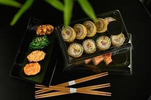 A luxurious spread of sushi and Japanese delicacies, served with precise elegance, awaits on a table set with dark plates and chopsticks. photo