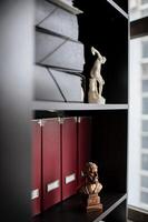 A bronze Aristotle statue is placed among rows of document folders in a professional office. photo