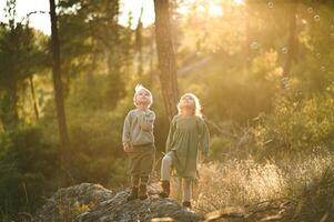 Two children stand in an enchanted forest, mesmerized by the glowing soap bubbles floating gently around them. photo