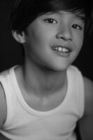 Against a deep black studio background, an Asian boy in casual attire gazes into the camera with a quiet, confident look photo