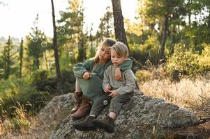A boy and girl sit on a mossy stone in an enchanted forest, surrounded by floating soap bubbles shimmering in the soft light. photo
