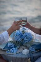 The gentle waves whisper against the shore, a candlelit dinner set beneath the vast blue sky, with wine reflecting the last light of day. photo