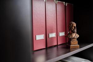 Stacks of labeled folders line the office shelves, with a statue of Aristotle adding a classic touch. photo