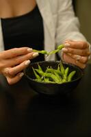 woman's hands gently pry open the fresh edamame pod, revealing the smooth green beans inside. photo