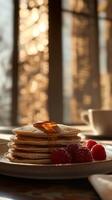 A stack of pancakes topped with syrup or honey and served with fresh raspberries. Warm natural light. Vertical image photo