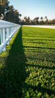 A racetrack scene with pristine racecourse with trimmed green grass. The white fence casting shadows on vibrant field photo
