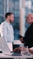 Multiracial happy, confident businessmen, teamwork brainstorm using on blurred background. Selective focus. Female hands typing on laptop computer at workplace. Corporate project software. Vertical video