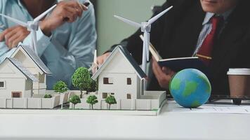 Two people sitting at a table with a model of a house and wind turbines video