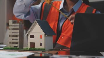 A woman in an orange vest is working on a model of a house video