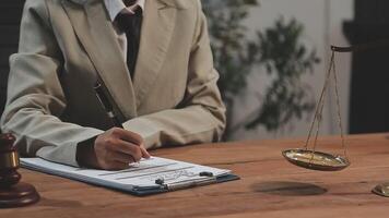 A woman in a suit writing on a notepad with a scale of justice video