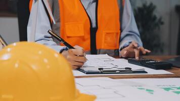 A person in an orange vest and hard hat sitting at a desk with a calculator and paper video