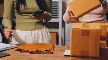 Two women are standing in front of boxes and a laptop video