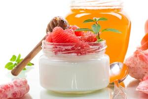 Diet breakfast. homemade sweet yogurt in a glass jar with pieces of red ripe grapefruit and honey, isolated on white background photo