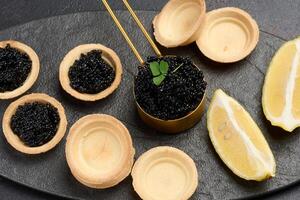 Black sturgeon caviar and empty round tartlets on table, top view photo