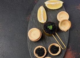 Black sturgeon caviar and empty round tartlets on table, top view. Close up photo