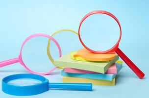 Multicolored plastic magnifying glasses on a blue background and paper notes. close up photo