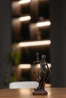 Golden lady justice statue is displayed on a wooden desk in a law office, symbolizing justice, fairness, and the legal system. Statue of Themis with a pair of scales of justice. Vertical shot photo