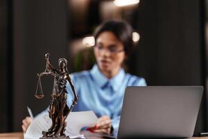 Statue of Justice with scales and a lawyer working on a laptop. Concept of legal consultations and decision-making using modern technology for efficient legal solutions photo