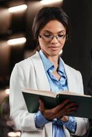 Black woman reading book in a library for education, studying and research in school, university or college campus. Focus, book and student at bookshelf for language learning or philosophy knowledge photo