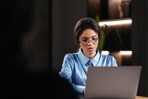Portrait of a Stylish African Female Student in Glasses Working on Her University Exercise on a Laptop Computer. Young Black Woman Studying an Online Course in an Empty Quiet Public Library photo