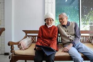 Senior asian couple are laughing and sitting on sofa while watching funny stand up comedy show from streaming digital tablet during winter time for mental health and happiness in marriage photo