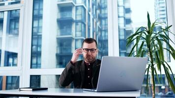 Smiling middle-aged man using laptop at office. Happy mature businessman send email and working. American freelancer typing on computer with paperworks and documents on table video