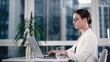 Woman, typing and computer for working in office, serious and keyboard for journalist, research and writing. Workplace, employee and person with laptop, planning and project for headline of article video