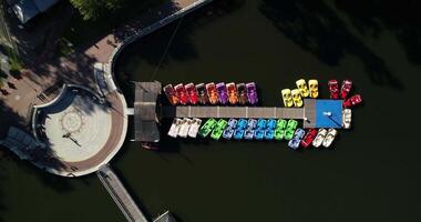 Colorful boats and catamarans for walking in the pond are moored on the pier, aerial view. Rental of catamaran boats for walks on the lake video
