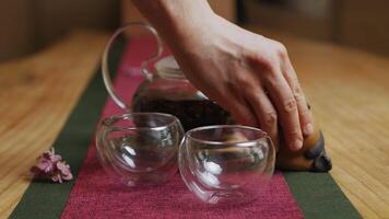 A serene setting with a glass teapot and cups on a wooden table. Media video