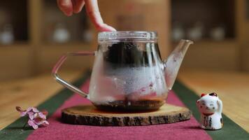A person pours steaming tea into a glass teapot on a rustic table. Media video