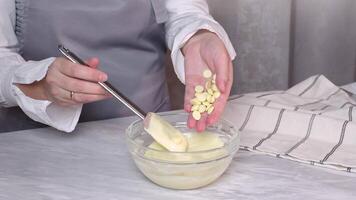 Adding white chocolate granules to a snow -white cream in a glass bowl with a spatula on a kitchen rack video