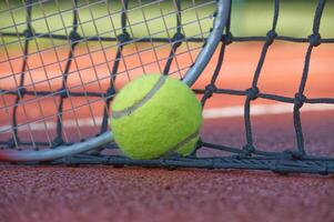 Tennis ball and racket resting on net of clay court photo