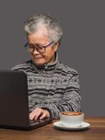 Senior woman uses a laptop to search for data from the internet while sitting at the table photo